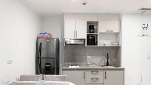 Una cucina moderna con frigorifero in acciaio inossidabile, macchina del caffè e lavandino. È presente un tavolo da pranzo con sottopiatti e bicchieri.