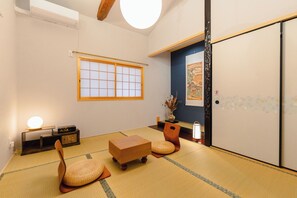 Una tradizionale stanza giapponese con pavimento in tatami, una porta scorrevole shoji, un tavolo basso in tatami, un mobiletto in legno basso e un tavolino con una lampada.