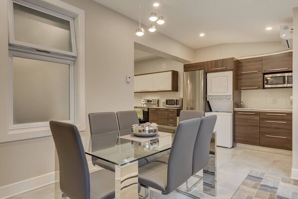 A modern kitchen with stainless steel appliances, wooden cabinets, and a glass dining table with chairs.