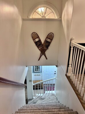 A staircase with a white railing, a heart-shaped wall decoration, and a view of a room with a door and a window.