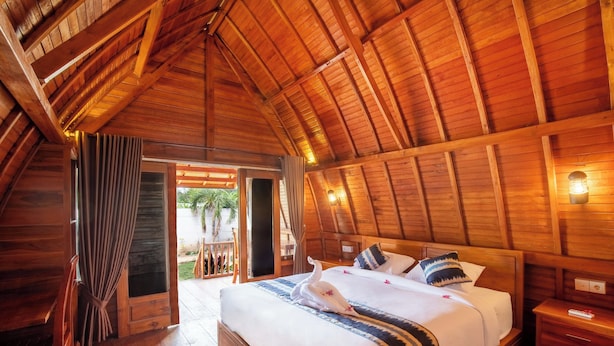 A wooden cabin bedroom with a large bed, wooden walls, and a sloped ceiling. - The Gili Menjangan (Pejarakan)