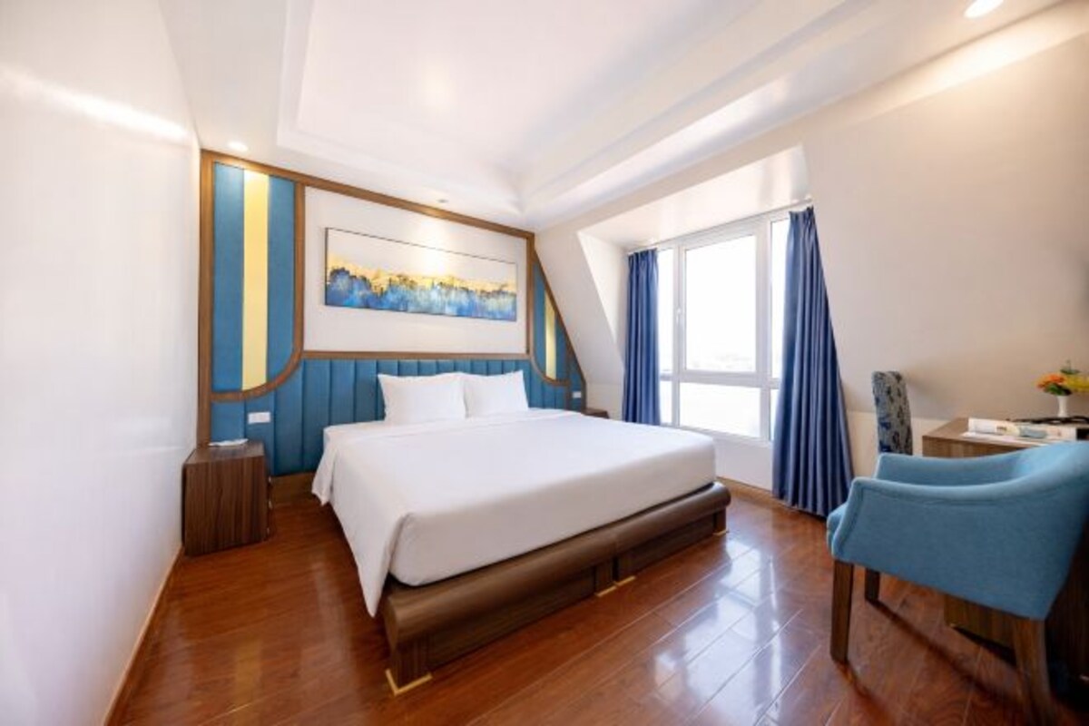 Habitación de hotel con una cama grande, un escritorio, una silla, un ventanal con cortinas y un cuadro en la pared.