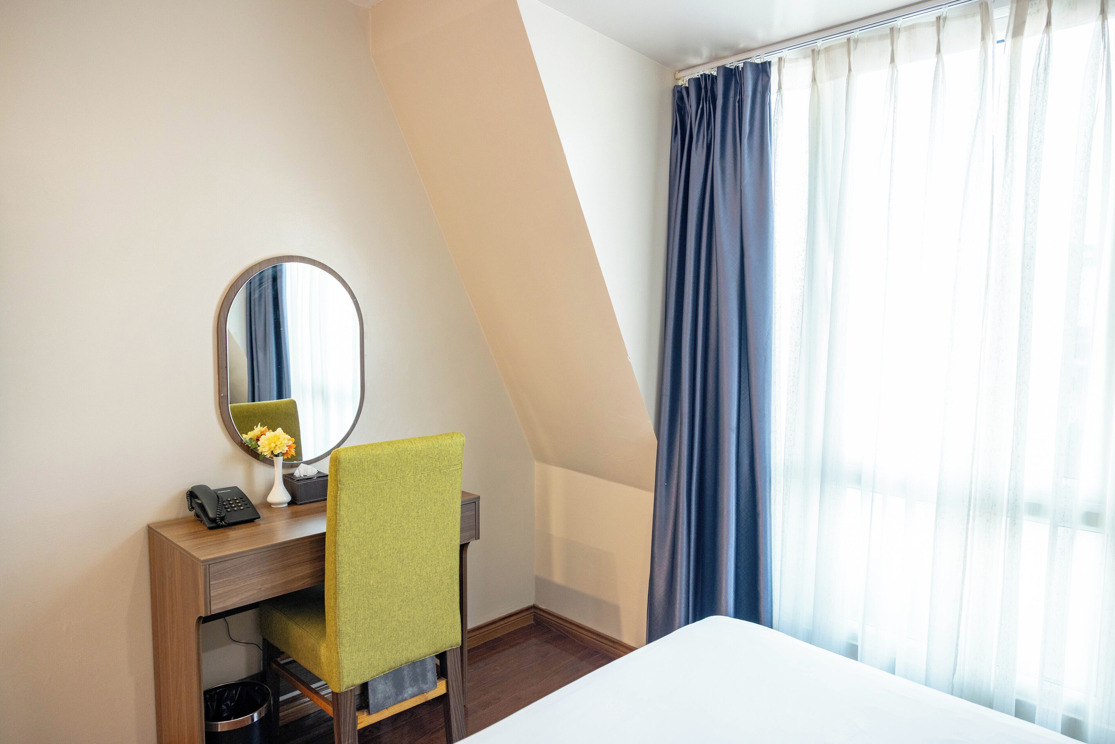A hotel room with a desk, chair, bed, and a large window with curtains.