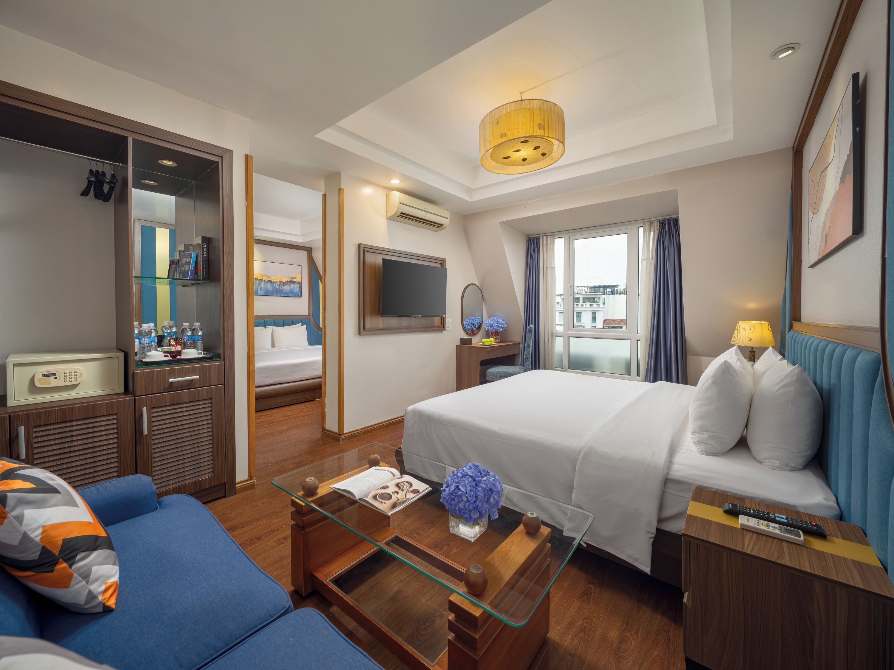 A hotel room with a bed, a sofa, a desk with a lamp, a TV, and a window with curtains.