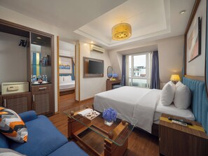 Habitación de hotel con cama, sofá, escritorio con lámpara, televisor y ventana con cortinas.