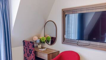 Una habitación con escritorio de madera, espejo, silla roja y ventana con vista al cielo.
