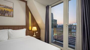 A hotel room with a bed, a nightstand, a lamp, and a large window with curtains.