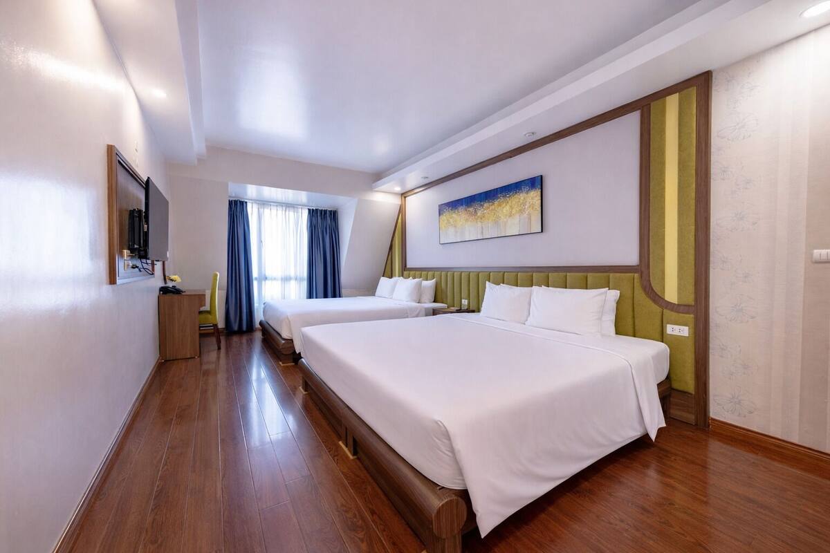 Une chambre d’hôtel avec deux lits, un bureau, une chaise et une fenêtre avec des rideaux.