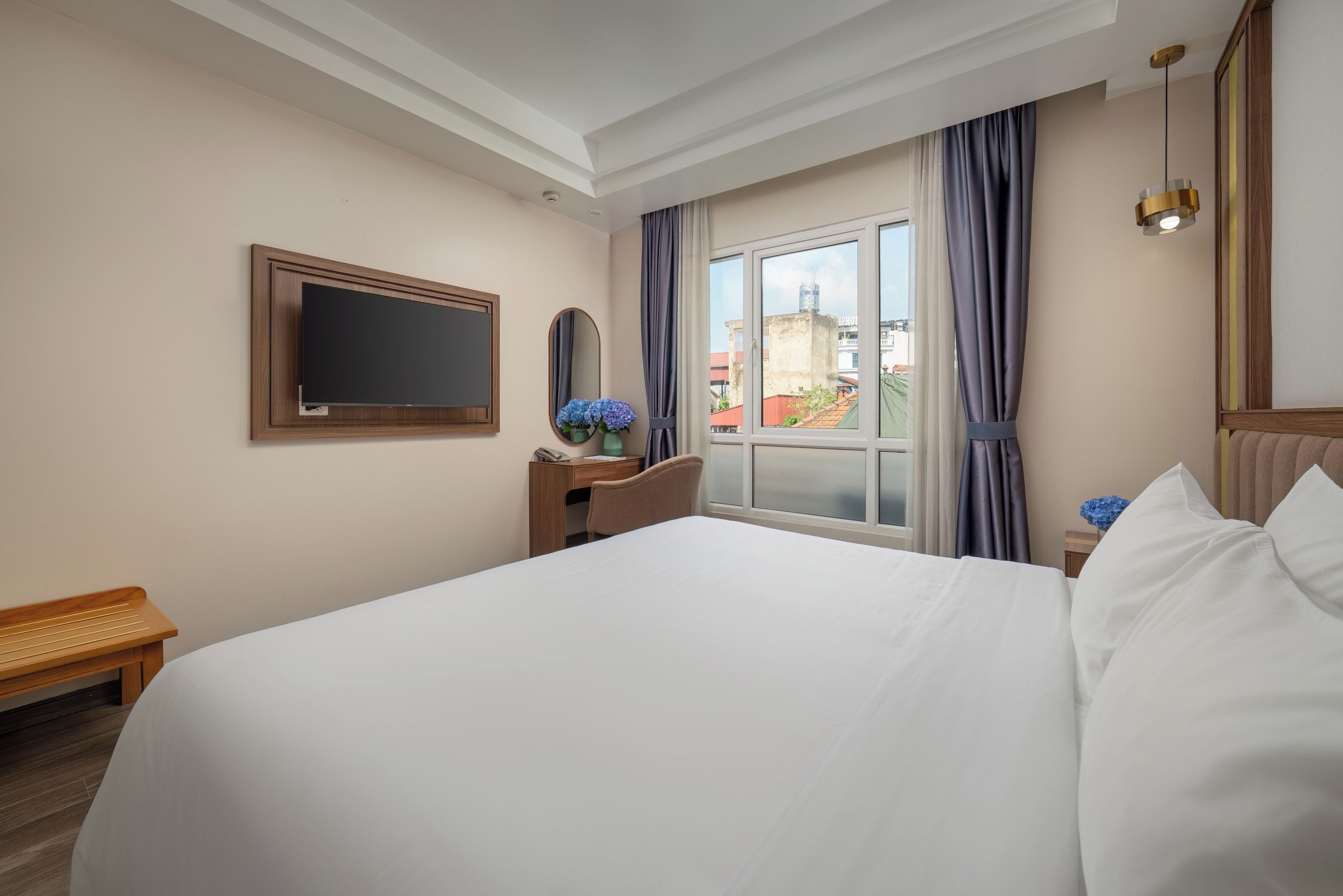 A hotel room with a large bed, a desk, a chair, a television, and a window with curtains.