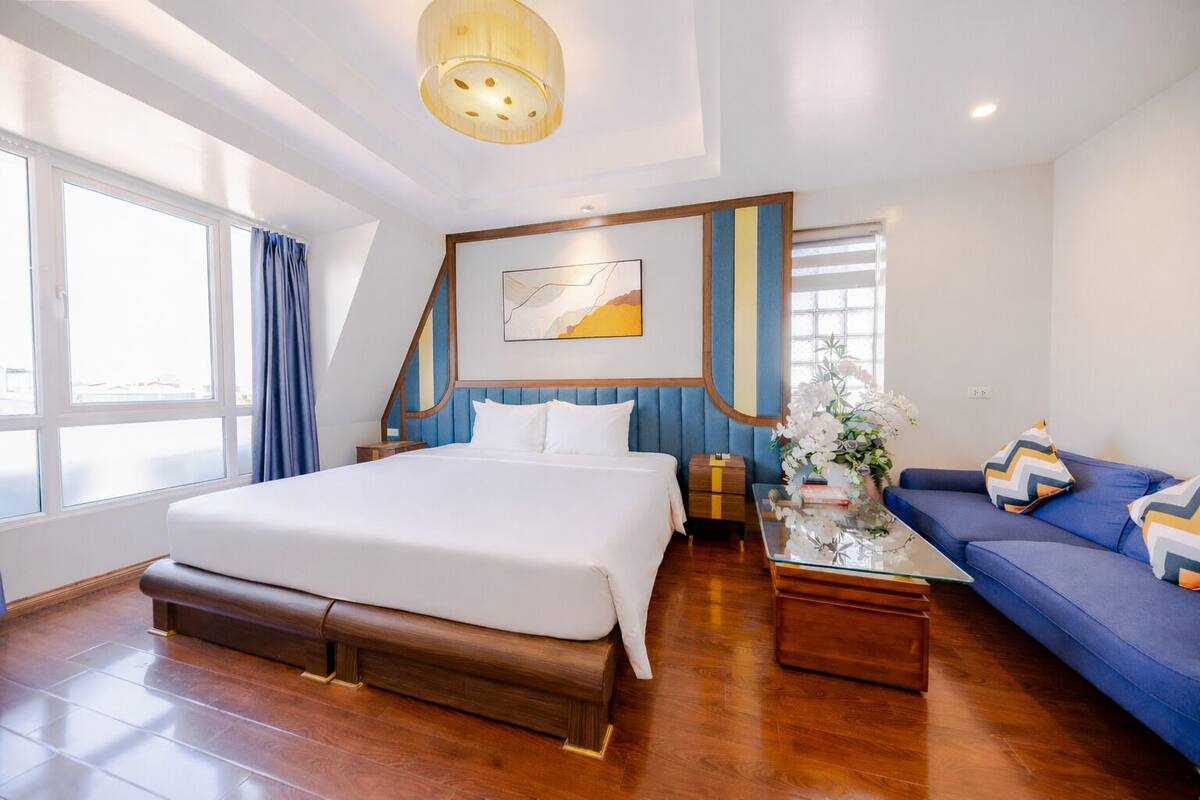 Une chambre d’hôtel moderne avec un grand lit, un canapé, une table basse en verre et une plante décorative.