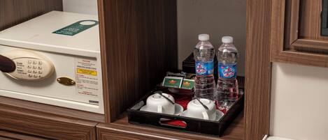 A hotel room with a minibar, a telephone, and a tray with bottles and cups.