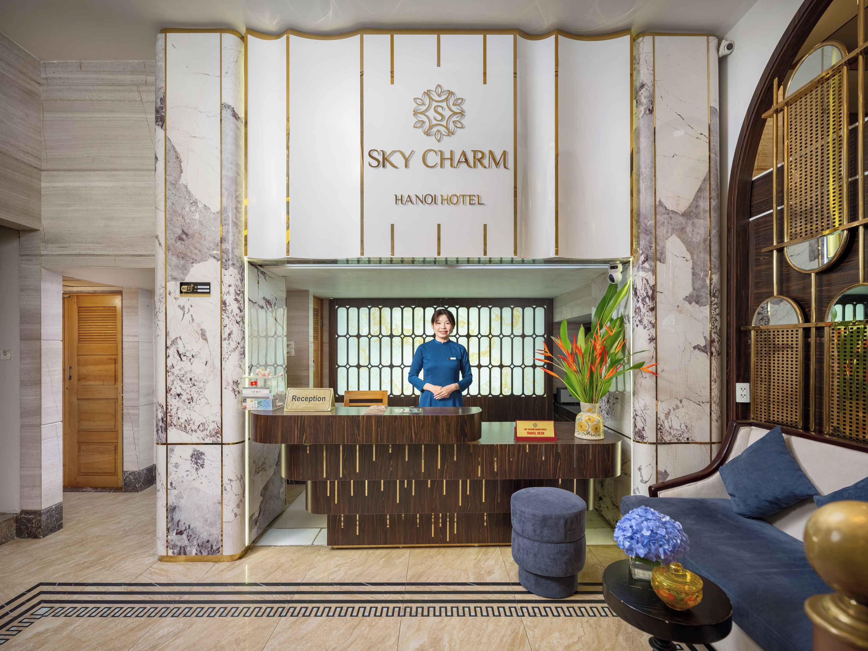 A hotel reception area with a marble reception desk, a receptionist, and a sofa with a vase of flowers.
