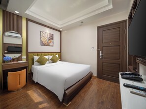 A hotel room with a bed, a desk with a chair, a television, and a door.