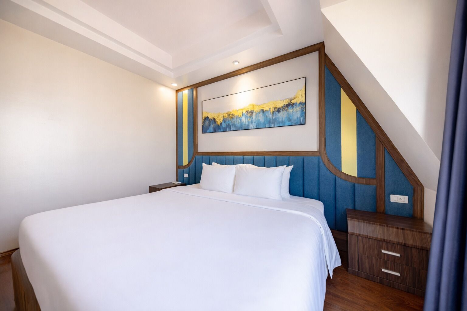 Een hotelkamer met een groot bed, een houten hoofdbord, een nachtkastje en een schilderij aan de muur.