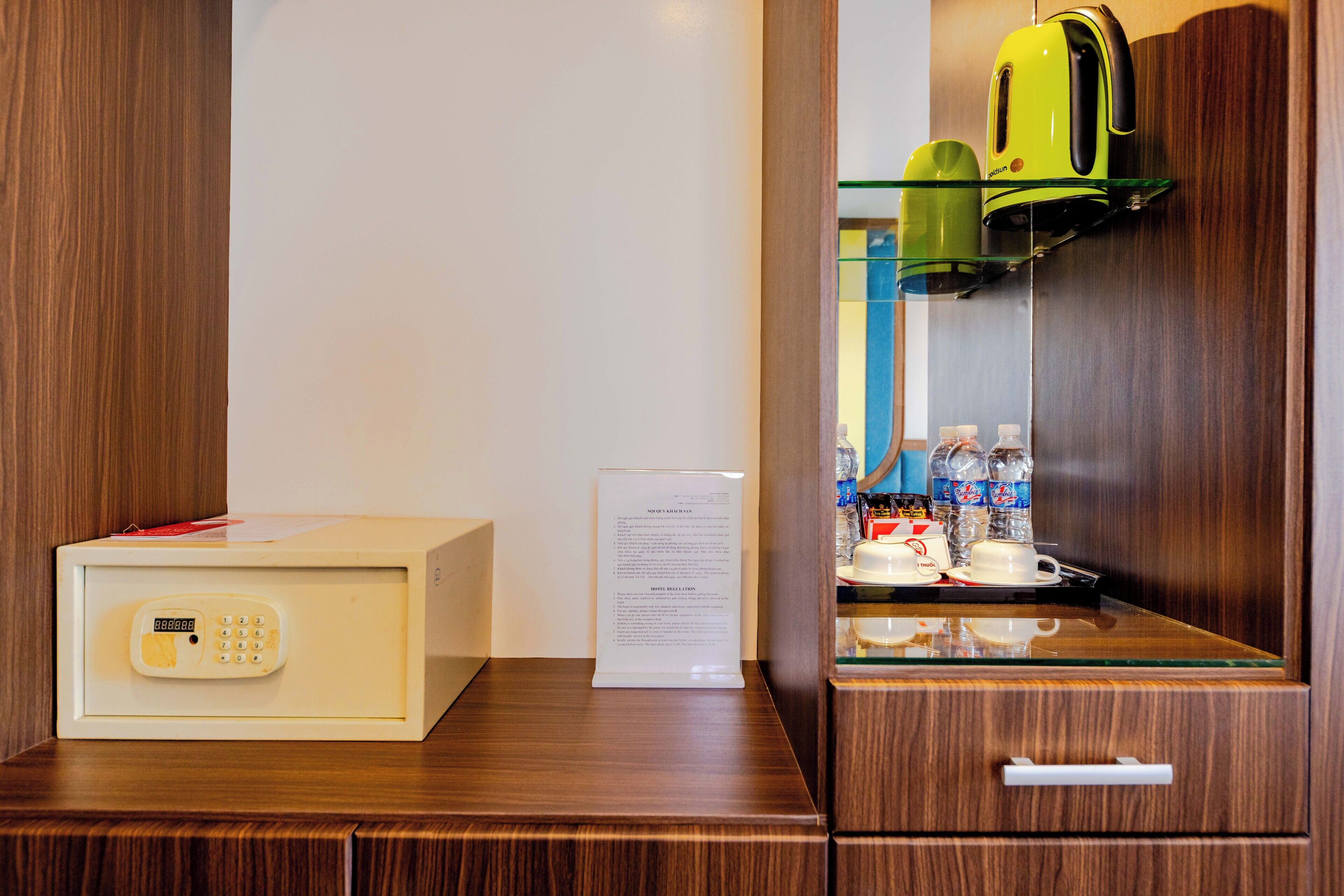 A hotel room with a minibar, a safe, and a glass display cabinet with bottled water and a kettle.