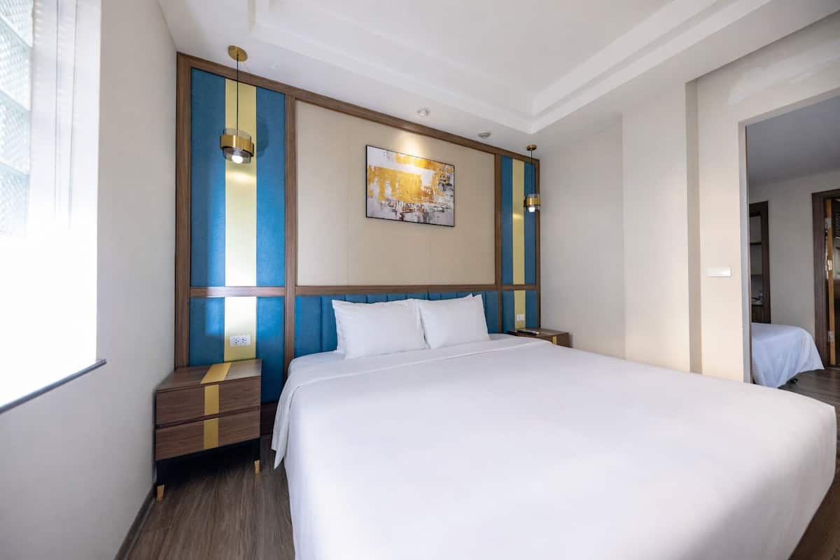 Une chambre d’hôtel avec un grand lit, une table de chevet, un tableau accroché au mur et une fenêtre avec des stores.