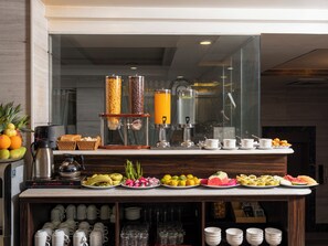 A breakfast bar with a coffee machine, a fruit display, and a variety of breakfast items.