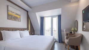 Habitación de hotel con una cama grande, un escritorio con silla, una ventana con cortinas y un cuadro en la pared.