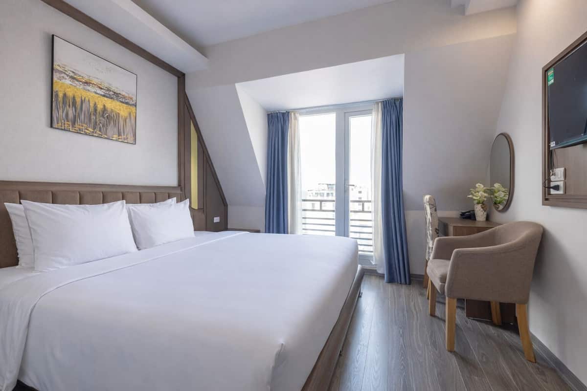 Une chambre d’hôtel avec un grand lit, un bureau avec une chaise, une fenêtre avec des rideaux et un tableau au mur.