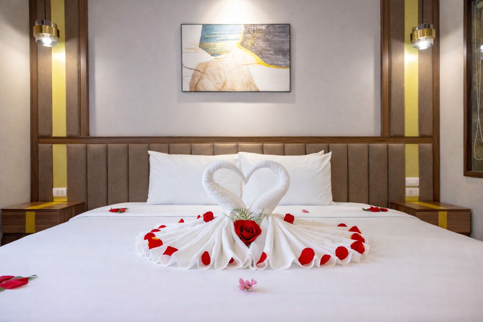 Una habitación de hotel con cama, una toalla dispuesta en forma de corazón y un cuadro en la pared.