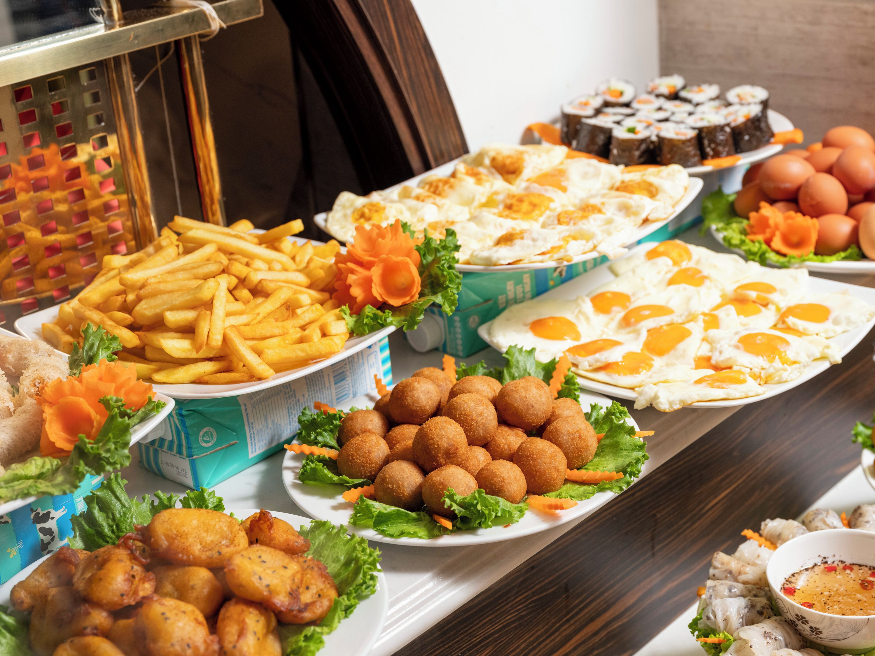 A buffet with various dishes including fried eggs, French fries, and meatballs.