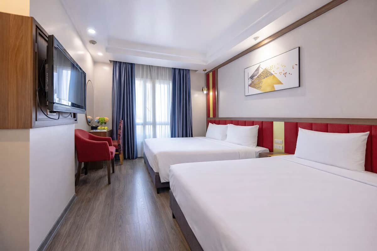 Une chambre d’hôtel avec deux lits, une télévision, un bureau avec une chaise et une fenêtre avec des rideaux.