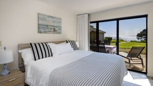 Ein Schlafzimmer mit einem großen Bett, einem Nachttisch, einem Fenster mit Meerblick und einem Stuhl davor.
