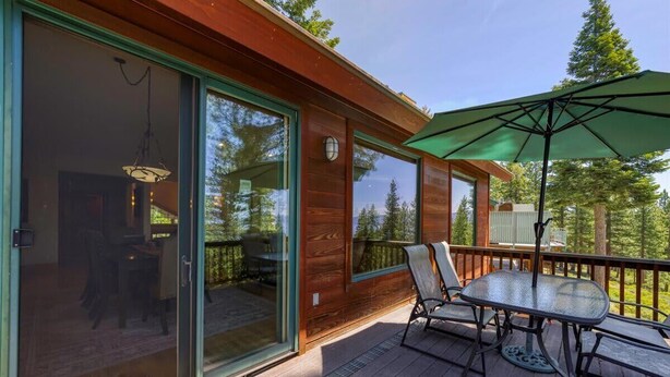 A wooden deck with a glass door leading to a room, a table with chairs, and an umbrella.