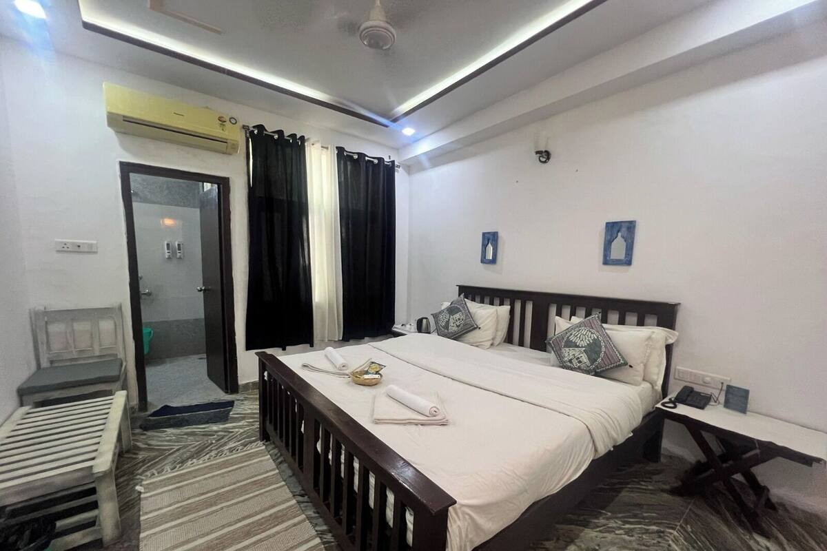 A bedroom with a bed, a bedside table, a chair, a shower area, and a door.