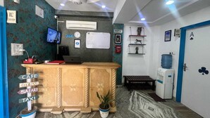 A reception area with a wooden counter, a clock, a television, and a water dispenser. - Thar View Hotel (Jaisalmer)