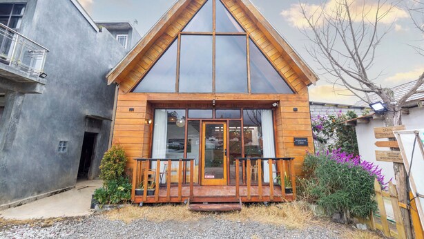 Una cabaña con fachada de madera, amplios ventanales de vidrio y una terraza de madera.
