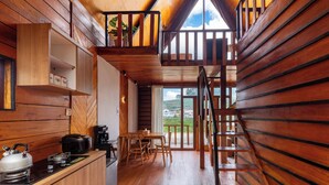 Interior de una cabaña de madera con cocina, comedor y un dormitorio en loft.