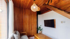 Una sala de estar acogedora con techo de madera, un sofá con cojines, una mesa de centro de madera y una lámpara colgante.