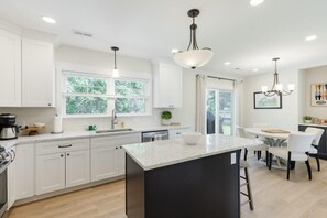 A modern kitchen with white cabinetry, a large island, and a dining area with white chairs.