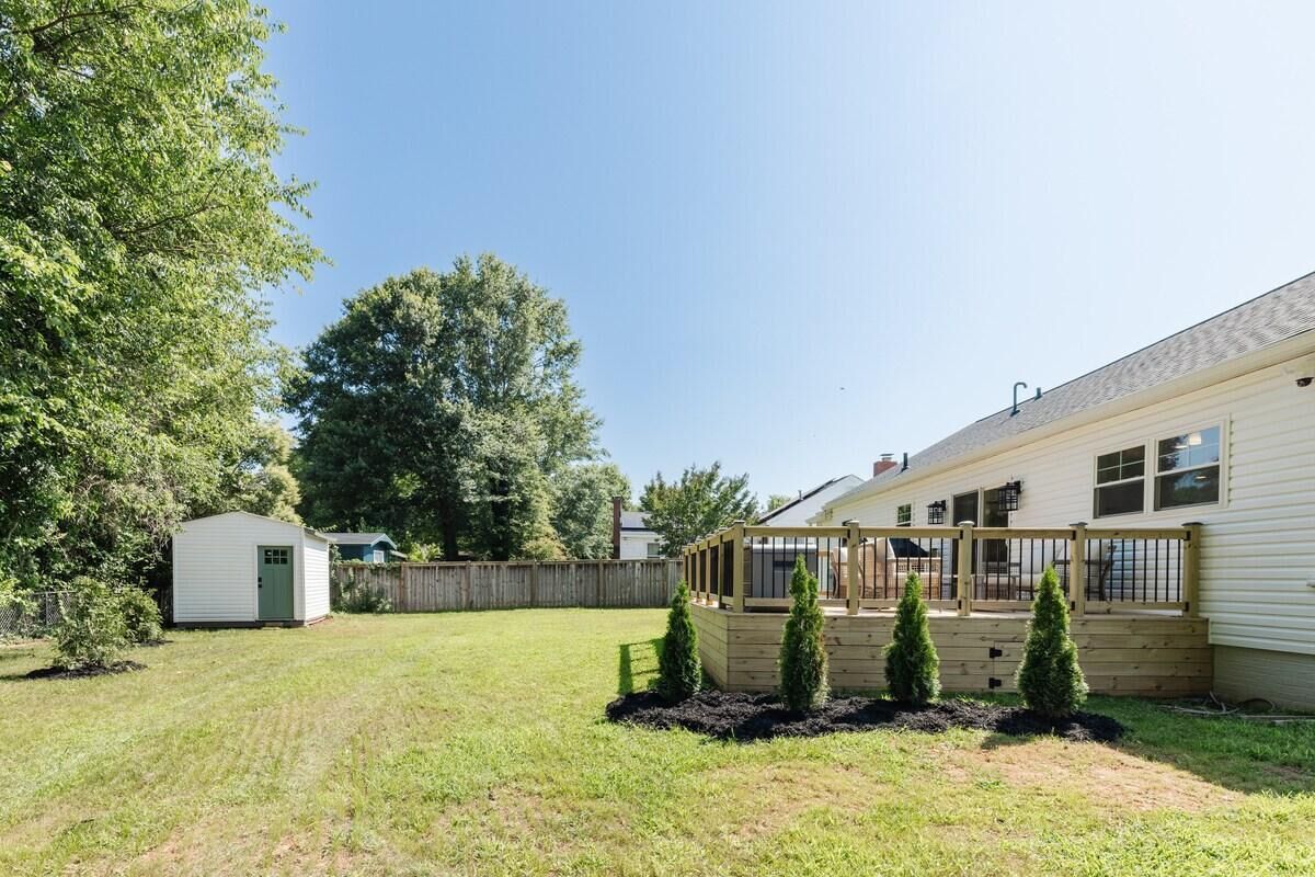 Un patio trasero residencial con una terraza de madera, un cobertizo y una casa.
