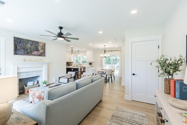 A modern living room with a grey sofa, a fireplace, a dining area, and a kitchen in the background.