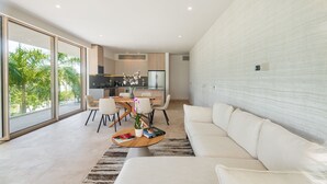 A modern living room with a white sofa, a dining area with a table and chairs, and a kitchen in the background. - Alba Puerto Cancún, Modern Lifestyle with Rooftop Near the Marina (Puerto Cancun)