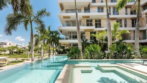 A swimming pool with a clear blue water, surrounded by palm trees and a multi-story building with balconies. - Alba Puerto Cancún, Modern Lifestyle with Rooftop Near the Marina (Puerto Cancun)