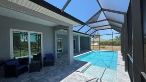 A covered outdoor swimming pool area with a patio, seating, and a view of the surrounding landscape. - Modern Villa 4BR/2BA heated pool near Boca Grande (Rotonda West)