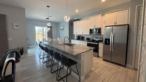 A modern kitchen with a central island, bar stools, stainless steel appliances, and pendant lighting. - Modern Villa 4BR/2BA heated pool near Boca Grande (Rotonda West)