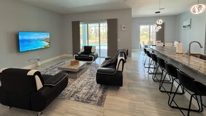 A modern living room with a flat-screen TV, a black leather sofa, a coffee table, and a dining area with bar stools. - Modern Villa 4BR/2BA heated pool near Boca Grande (Rotonda West)