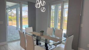 A modern dining area with a glass table and white chairs, large windows, and a pool view. - Modern Villa 4BR/2BA heated pool near Boca Grande (Rotonda West)