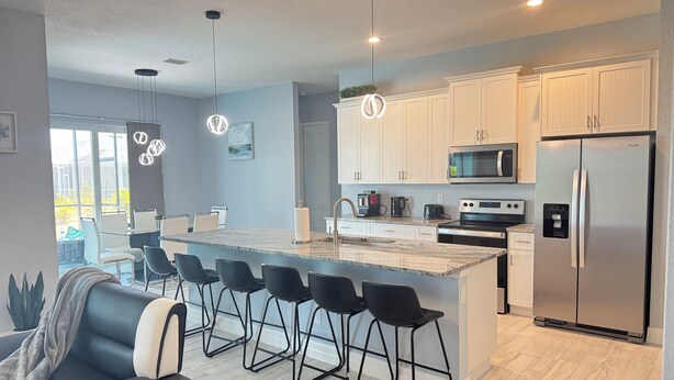 A modern kitchen with a central island, bar stools, stainless steel appliances, and pendant lighting. - Modern Villa 4BR/2BA heated pool near Boca Grande (Rotonda West)