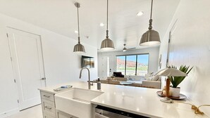 A modern kitchen with a large island, stainless steel dishwasher, and pendant lighting.