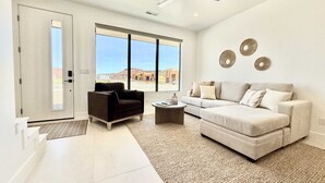 A spacious living room with a large window, a ceiling fan, and a beige sofa.