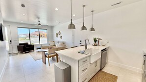 A modern kitchen with a central island, pendant lighting, and a view of the outdoors through large windows.