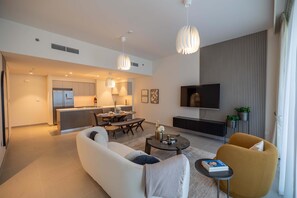 A modern living room with a sofa, coffee table, and yellow armchair. There is a kitchen in the background with a dining area.