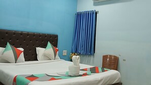 A hotel room with a bed, a ceiling fan, an air conditioning unit, and a window with blue curtains. - Hotel Mahaveer Paradise Bilaspur (Bilaspur)