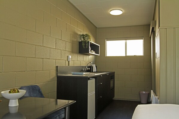 A compact kitchen with a sink, stove, and a small countertop. There is a window providing natural light and a plant on the wall. - Aqua Bella Motel (Napier)