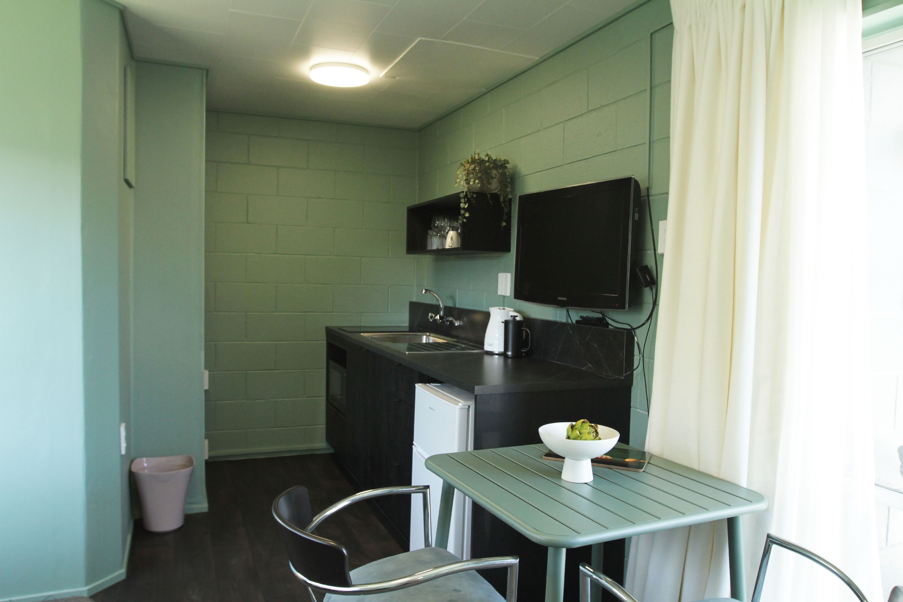 A compact kitchen with a sink, a small refrigerator, a microwave, and a table with chairs.